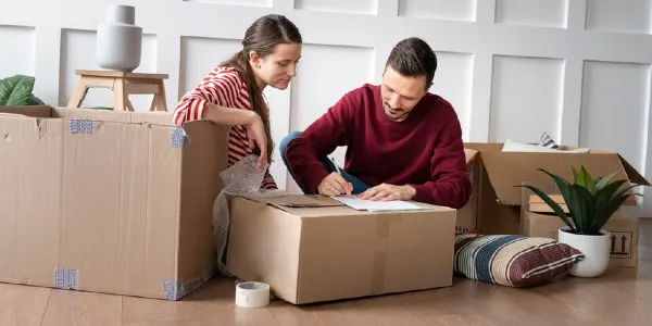 A man is writing something on a paper with moving boxes all around.